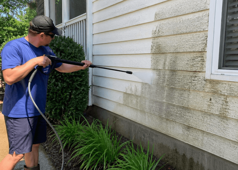 person pressure washing exterior house siding to remove dirt and mold buildup